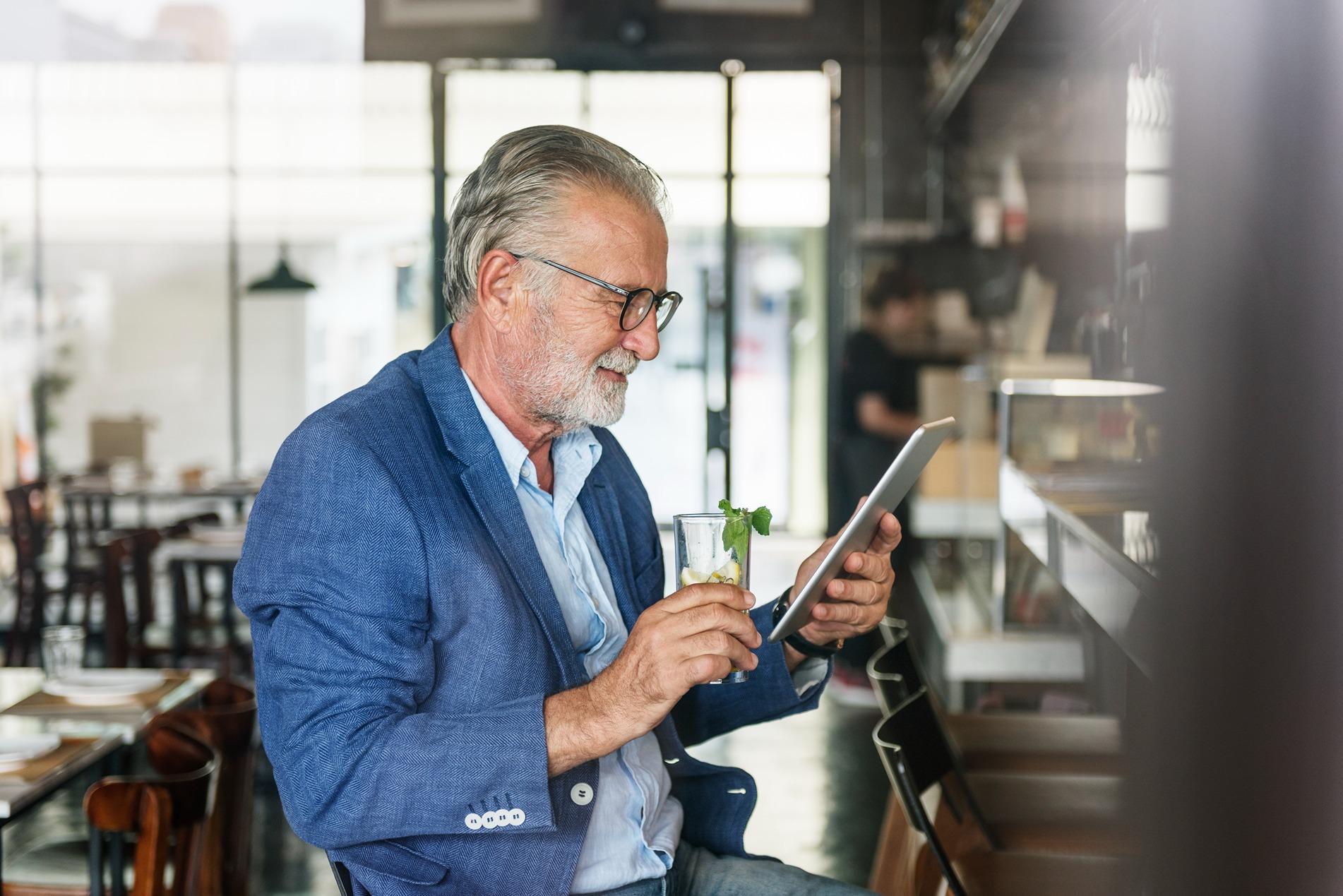 Resengo - Un homme est assis au bar avec un verre et regarde sa tablette.