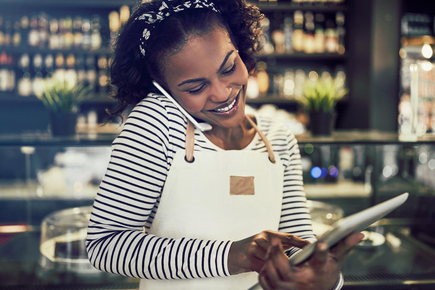 Resengo - Lachende vrouw hangt aan de telefoon terwijl ze een order ingeeft op haar tablet.